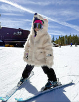 Kid skiing on a snowy slope with a clear blue sky wearing a polar bear coat costume.
