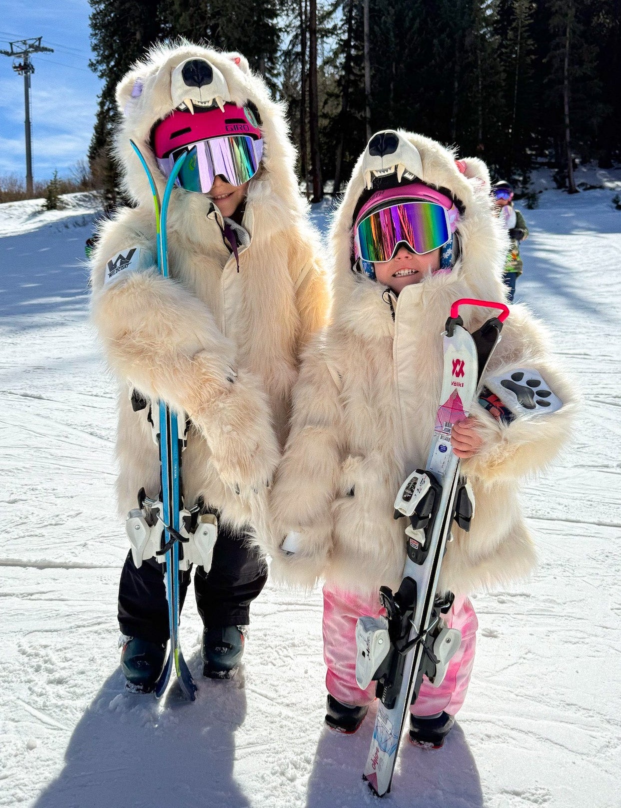Two children in warm bear coat costumes holding skis on a snowy slope at the ski resort.