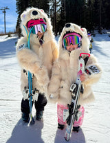 Two children in warm bear coat costumes holding skis on a snowy slope at the ski resort.