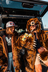 Two chicago bears fans celebrating at a tailgate by cheersing their beverages. Both are wearing wildcoat grizzly bear coats