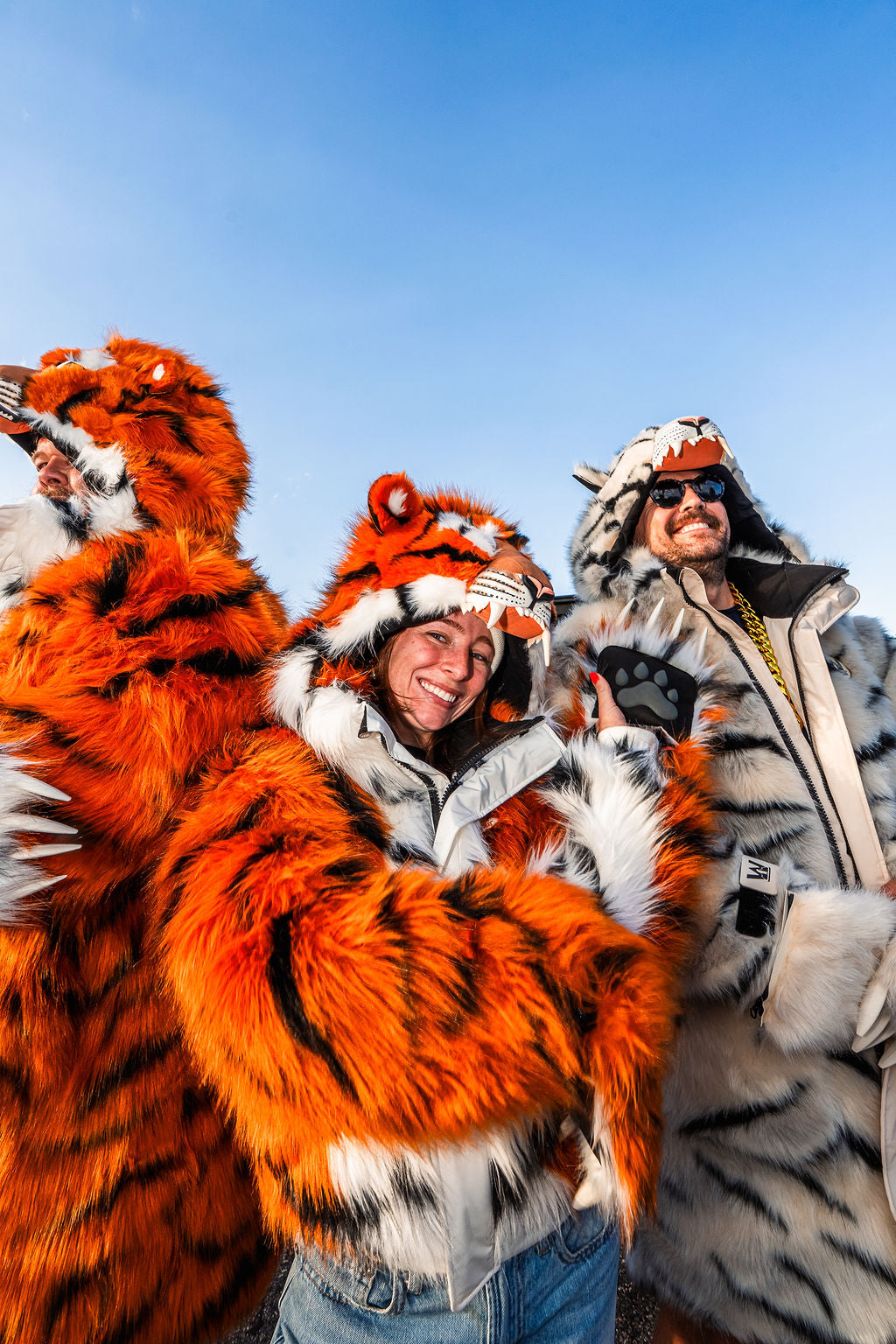 Woman Cincinnati Bengals fan wearing the wildcoat orange bengal tiger bomber at a tailgate, surrounded by two men wearing the orange bengal tiger parka and the white tiger parka