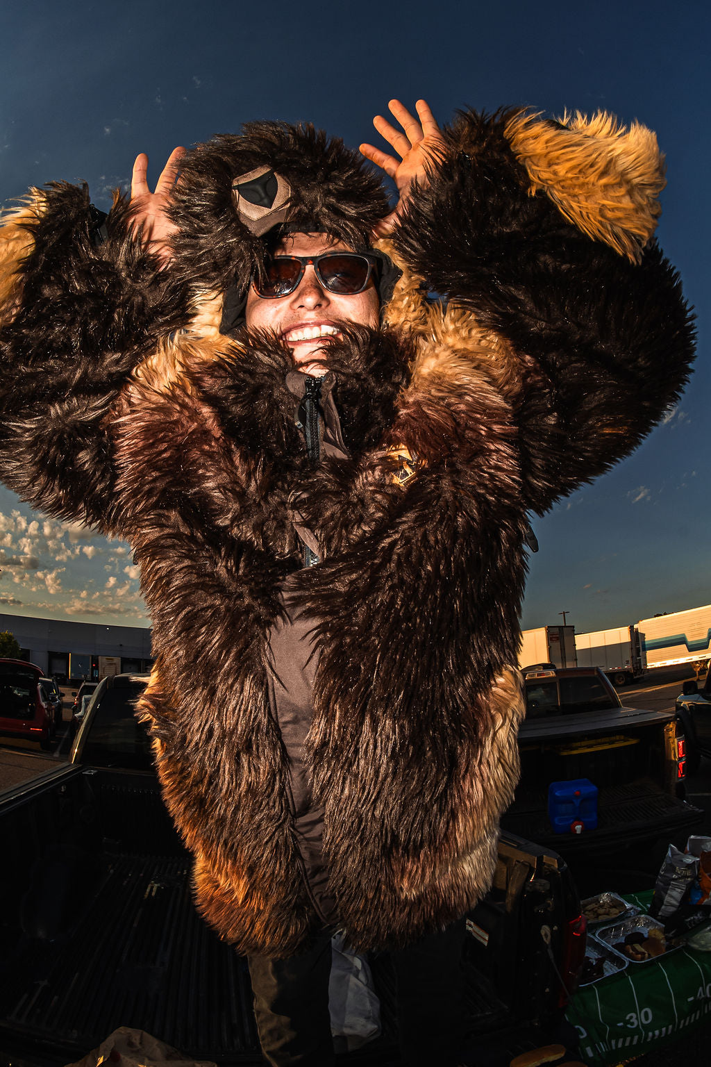A man wearing a wildcoat great white buffalo coat holds the horns of the coat while at a tailgate