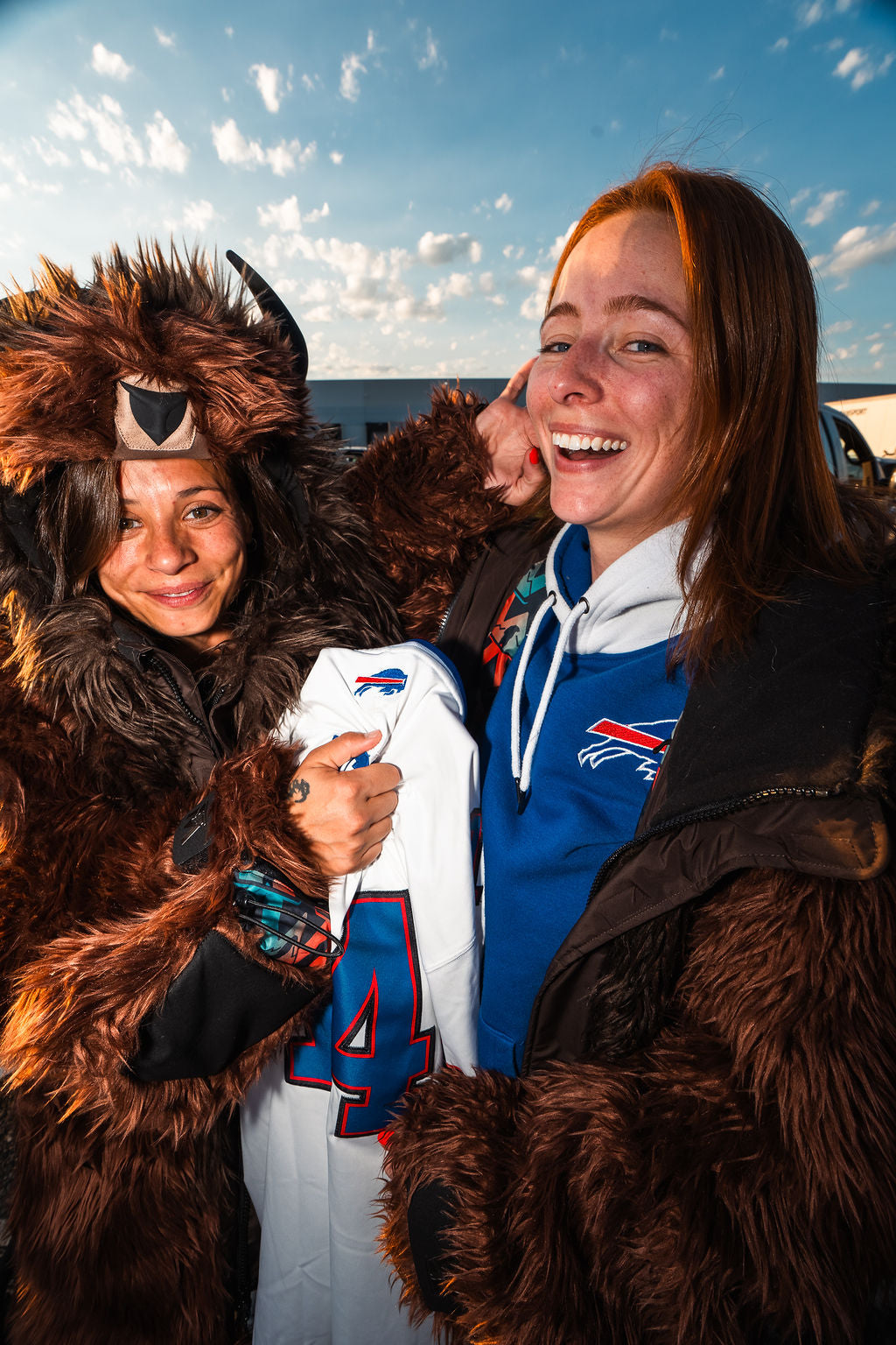 Two people posing at a buffalo bills tailgate, both are wearing wildcoat brown buffalo coats and buffalo bills gear