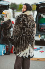 A woman wearing a large mottled animal-print fur Wildcoat eagle parka coat with a cream fur collar, standing outdoors at what appears to be a Philadelphia Eagles tailgate