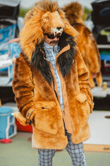 A person wearing an oversized lion costume jacket with a realistic lion head hood, tan and brown faux fur, and a dark mane, standing outdoors in a street or market setting at a detroit lions tailgate