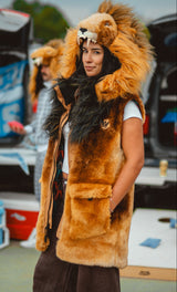 A woman wearing a plush lion costume vest with a large furry hood featuring a lion face and mane, standing outdoors near vehicles and coolers at a detroit lions tailgate