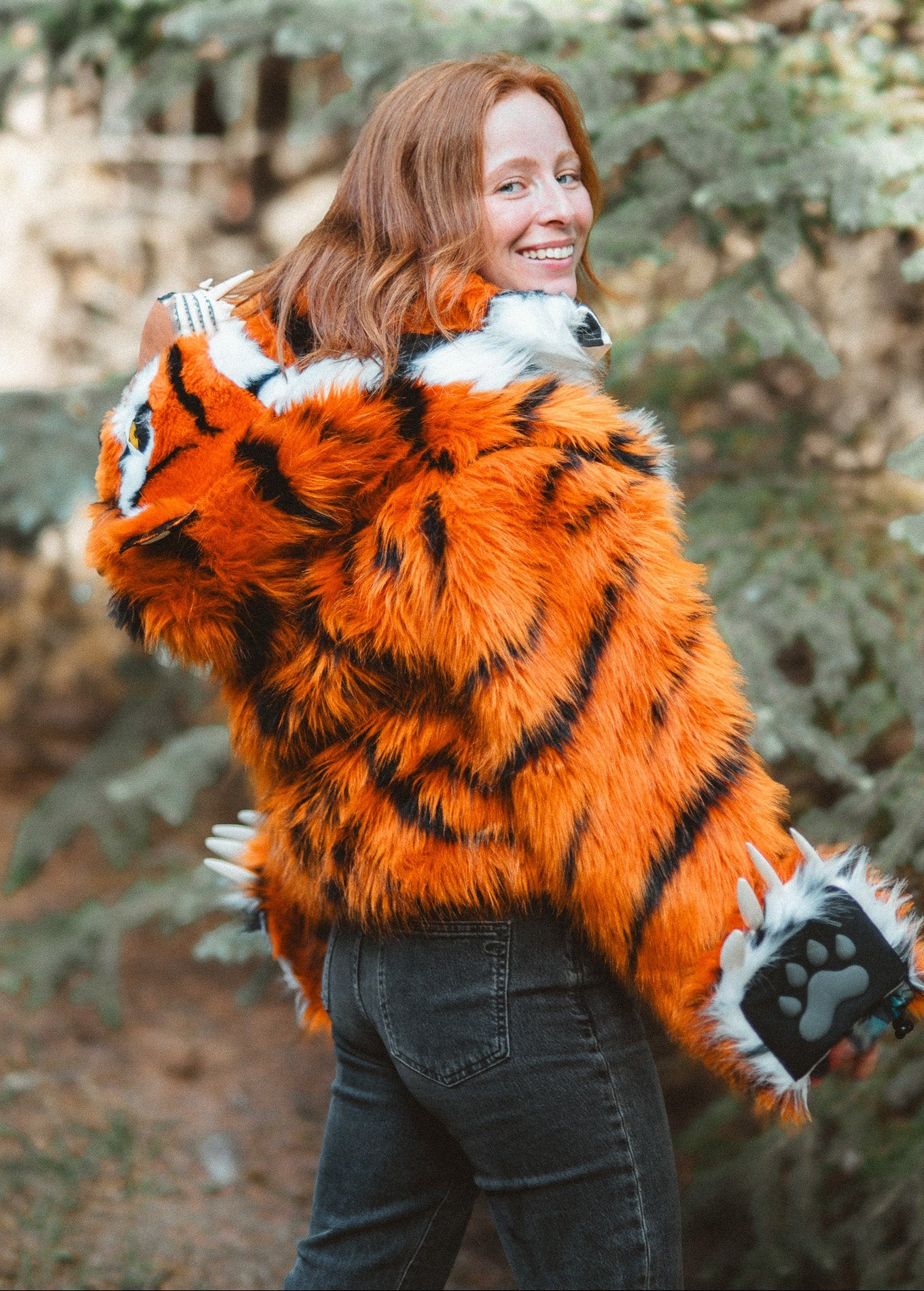 Smiling Woman wearing new v6 wildcoat orange tiger bomber with the hood down, mittens magnetically connected to the wrists.