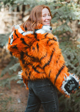 Smiling Woman wearing new v6 wildcoat orange tiger bomber with the hood down, mittens magnetically connected to the wrists.