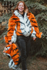 Woman wearing wildcoat orange tiger bomber coat jacket, carrying the detachable hood in her hand while smiling