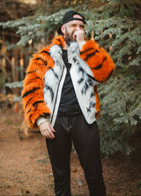 A man wearing a vibrant orange and black tiger-striped faux fur jacket with a white and black spotted pattern on the front, standing in a forest setting.