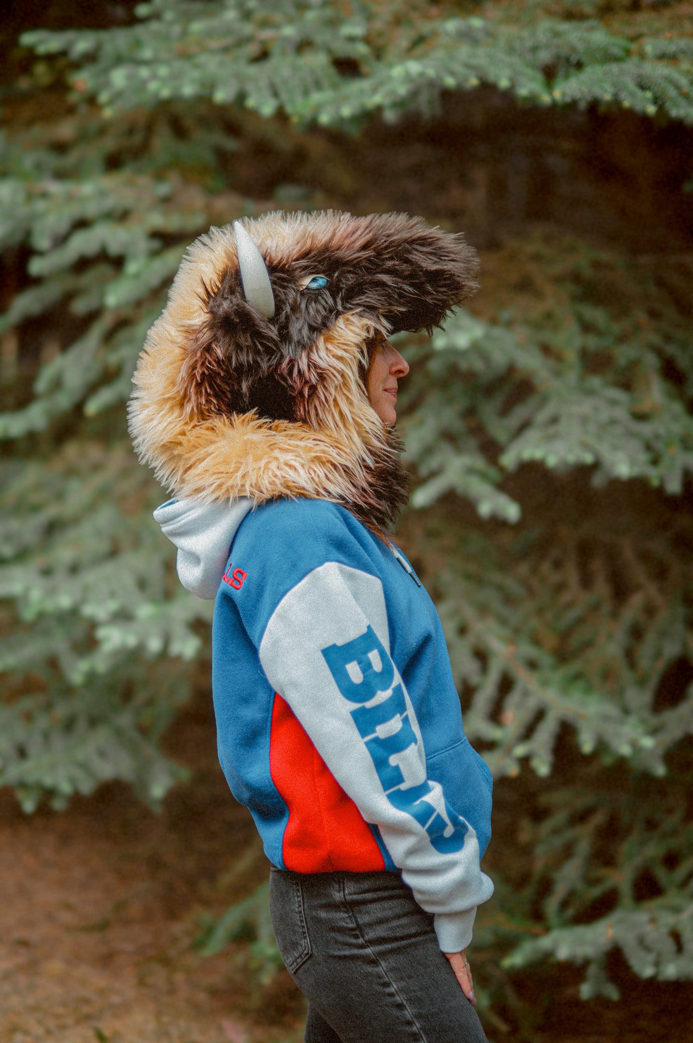 Woman wearing the wildcoat great white buffalo hood showing the full side profile, including bone-colored horn and bright blue eye