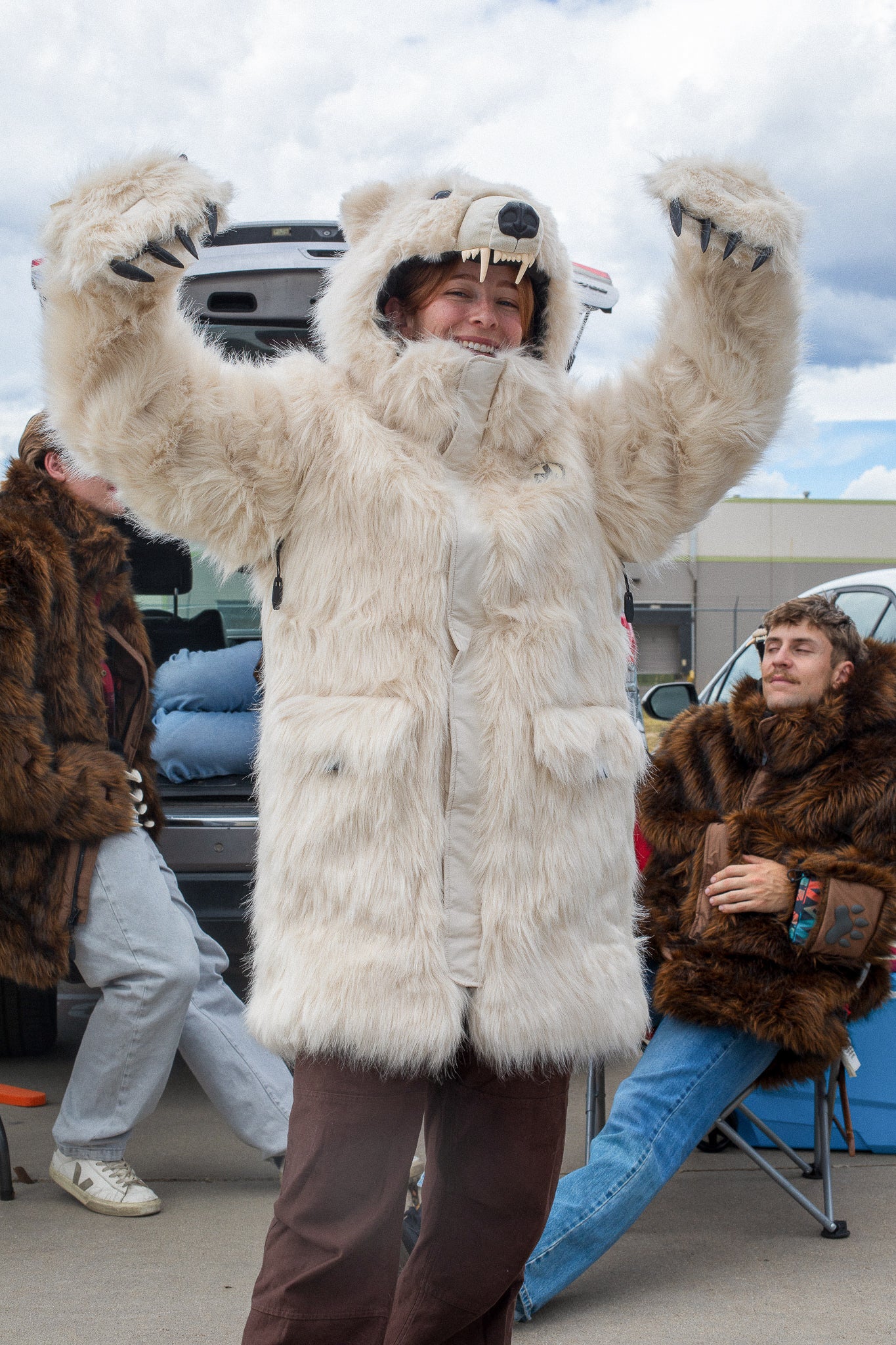 woman wearing a faux fur polar bear parka at a bears tailgate, showing off her clawed mittens with her arms raised