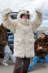 woman wearing a faux fur polar bear parka at a bears tailgate, showing off her clawed mittens with her arms raised