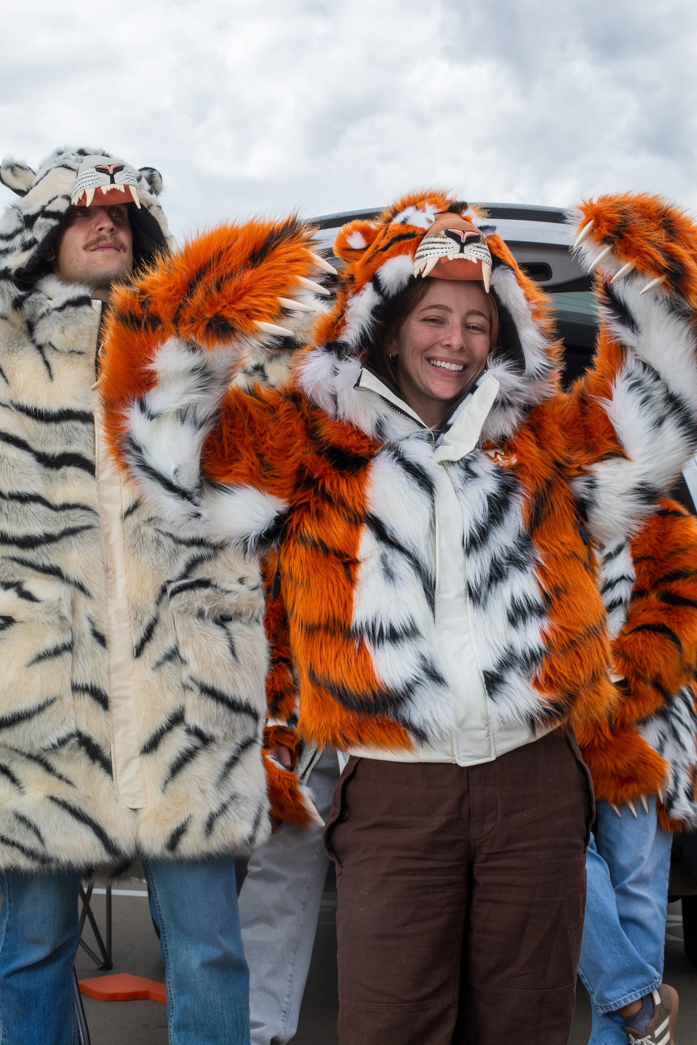 woman wearing a wildcoat faux fur orange bengal tiger bomber-cut coat / jacket. man on her left is wearing a white bengal tiger parka length faux fur coat 