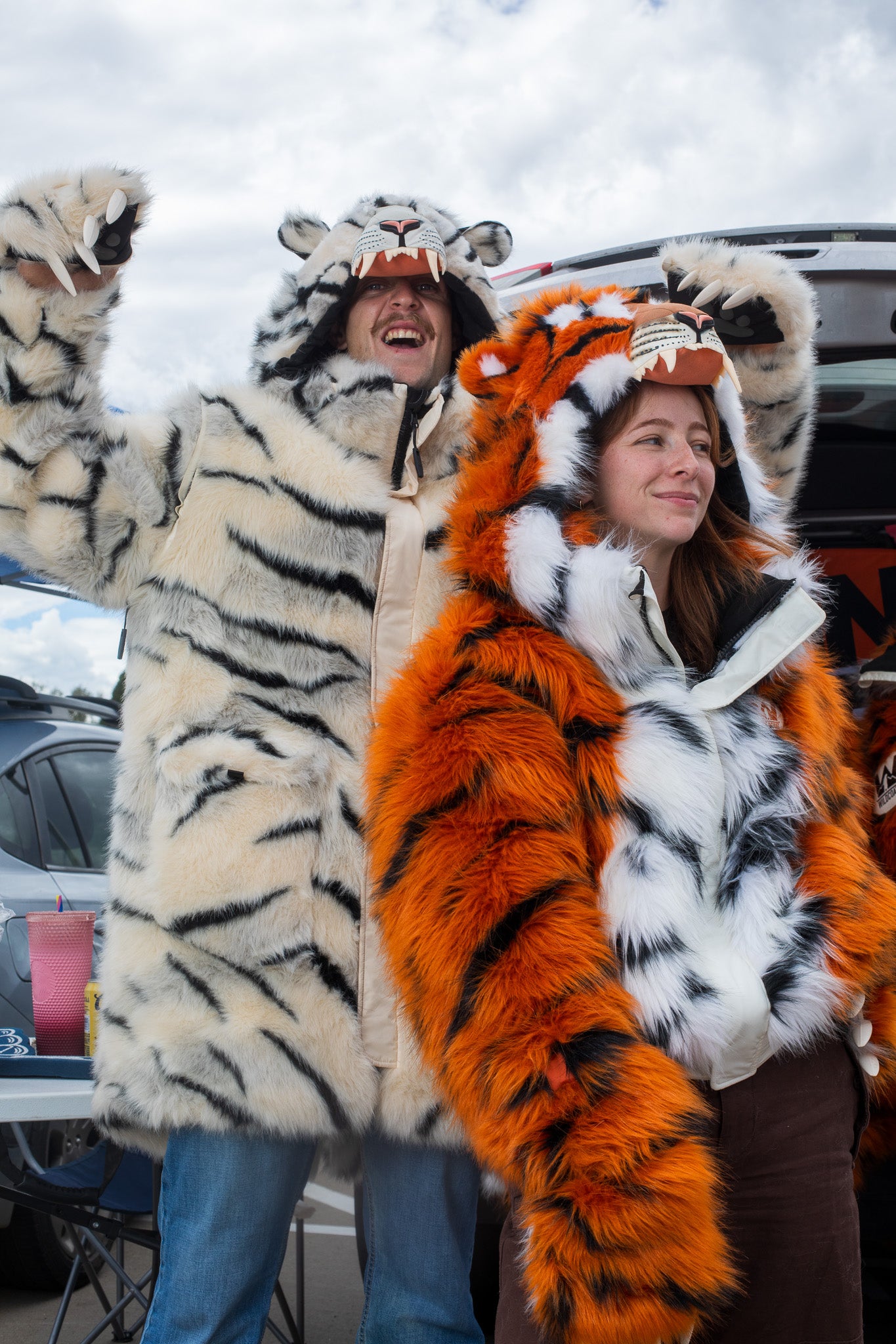 woman wearing a wildcoat faux fur orange bengal tiger bomber-cut coat / jacket. man on her left is wearing a white bengal tiger parka length faux fur coat 