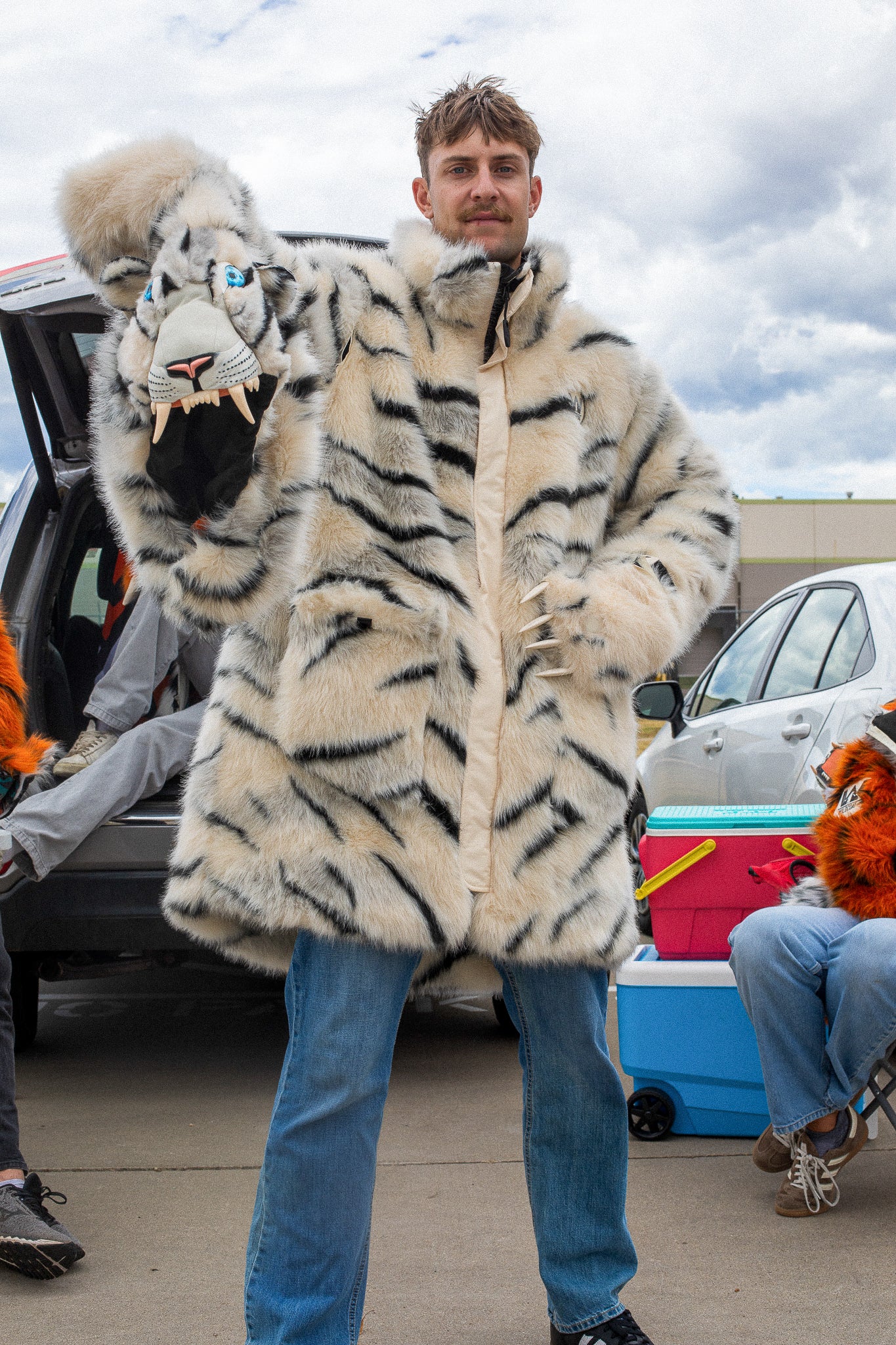 man wearing a wildcoat faux fur white bengal tiger coat, the hood is zipped off and hes holding it up to the camera in his right hand