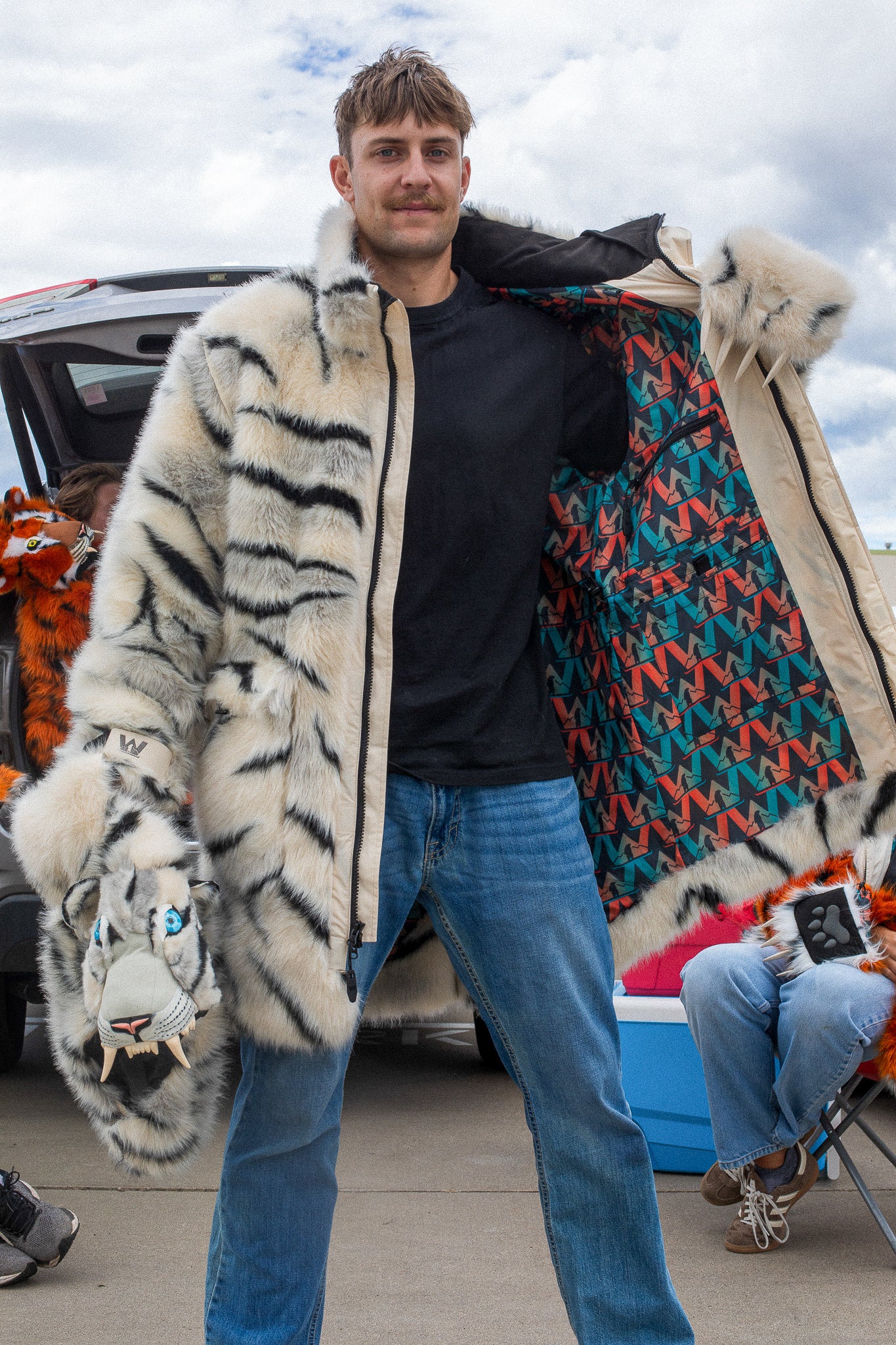 man wearing a wildcoat faux fur white bengal tiger coat, hes holding the coat open to show the wildcoat branded inner liner and holding the hood in his right hand