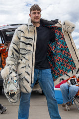 man wearing a wildcoat faux fur white bengal tiger coat, hes holding the coat open to show the wildcoat branded inner liner and holding the hood in his right hand