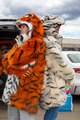 two men standing back to back, one is  wearing a wildcoat orange tiger faux fur parka coat at a tailgate, the other is wearing a wildcoat white tiger faux fur parka coat. both have their hoods up