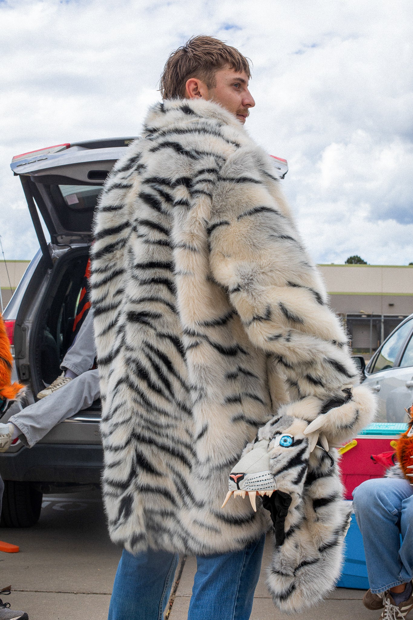 man wearing a wildcoat faux fur white bengal tiger coat, facing away with the hood zipped off and held in his right hand