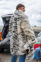 man wearing a wildcoat faux fur white bengal tiger coat, facing away with the hood zipped off and held in his right hand