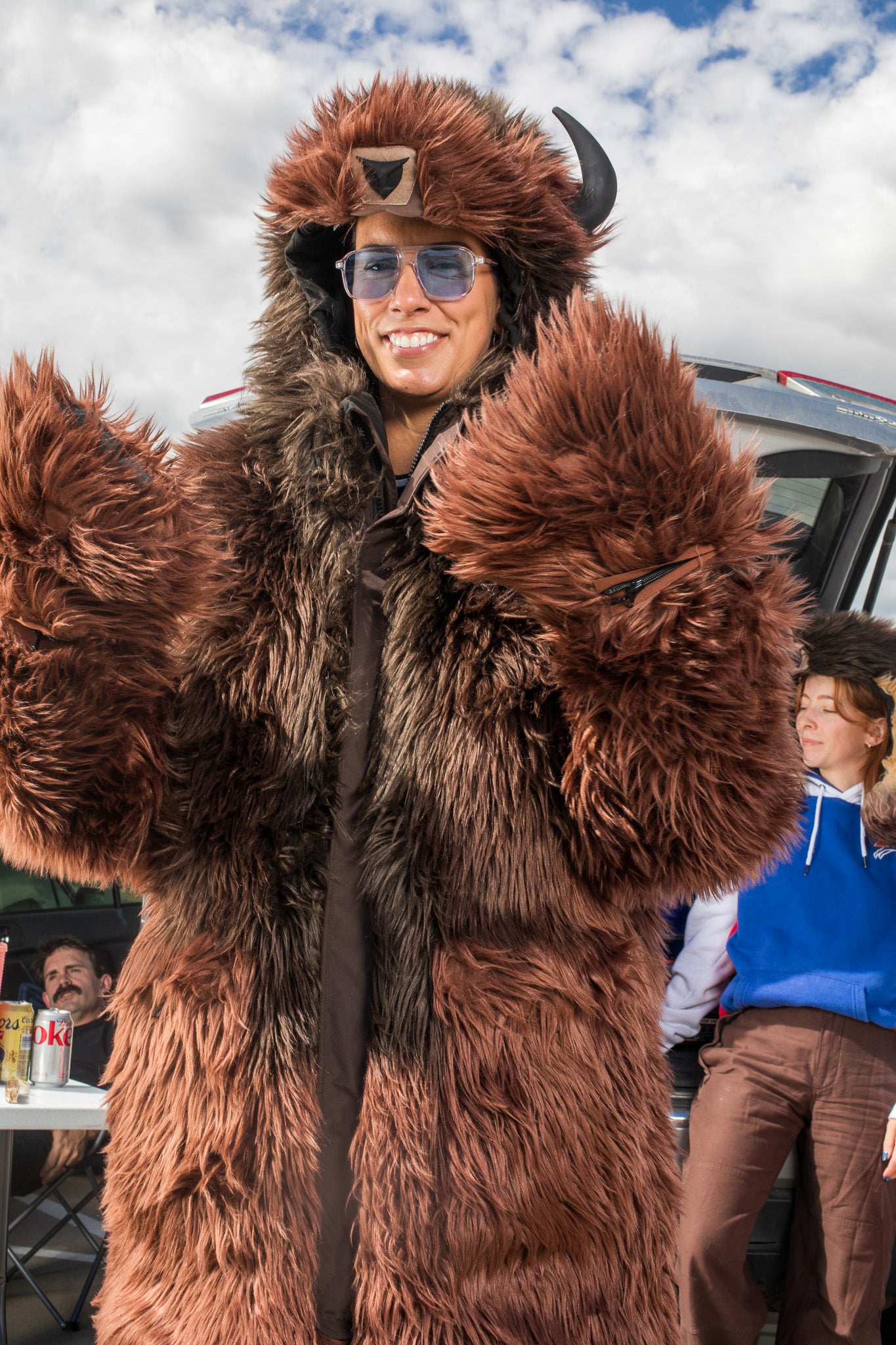 woman wearing a wildcoat v6 buffalo bison faux fur winter coat at a tailgate with a woman in the background wearing the great white buffalo hood
