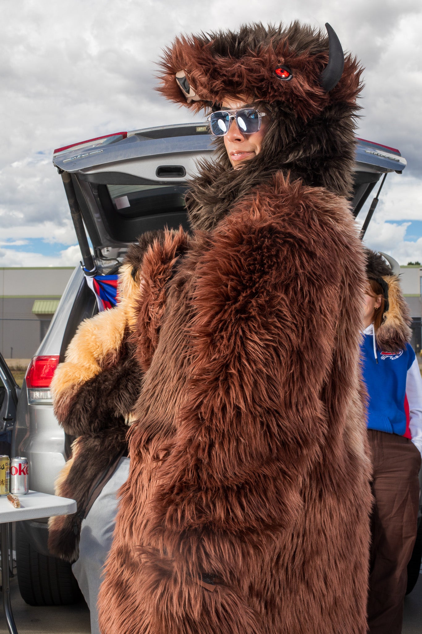 woman wearing a wildcoat v6 buffalo bison faux fur winter coat at a tailgate with a man in the background wearing the great white buffalo coat, and a woman in the background is wearing the great white buffalo hood