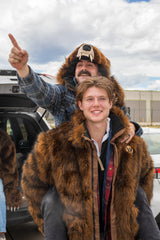 man wearing a faux fur grizzly bear hood helmet head cover at a tailgate while riding on the back of a man wearing a hoodless wildcoat grizzly bear parka coat
